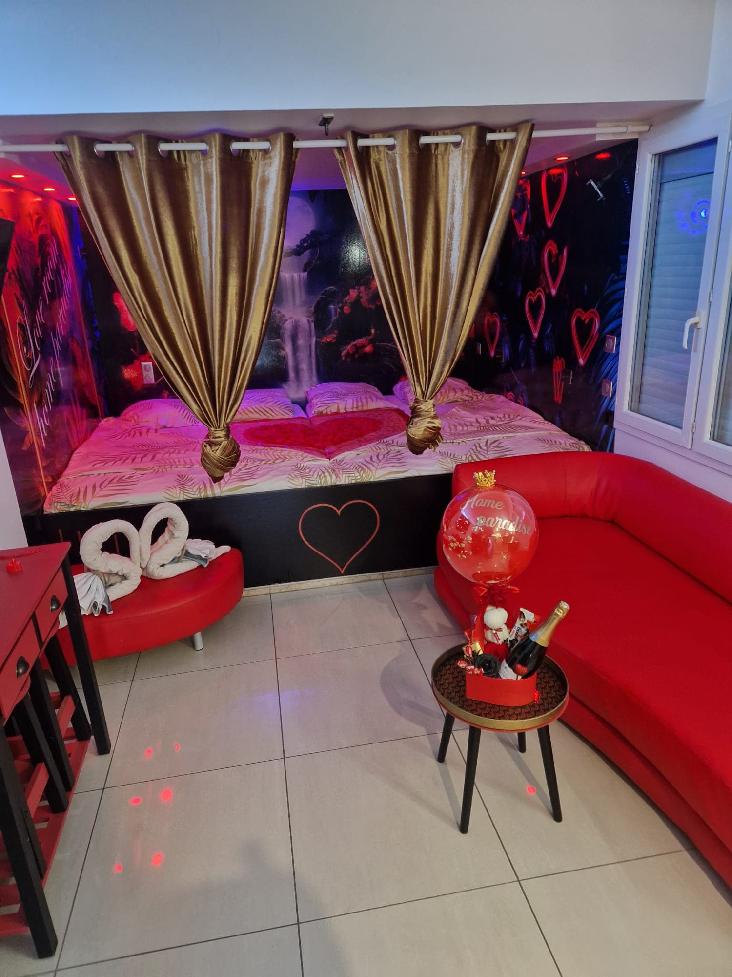 Chambre romantique, lit aux cœurs, canapé rouge, champagne et décoration lumineuse